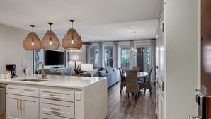 A modern kitchen with a central island, pendant lights, and a dining area with a round table and chairs. - Bayfront Serenity: 1 Bedroom, 2 Baths, Sunset Views, Private Balcony at Sandestin Golf and Beach Resort! (Miramar Beach)