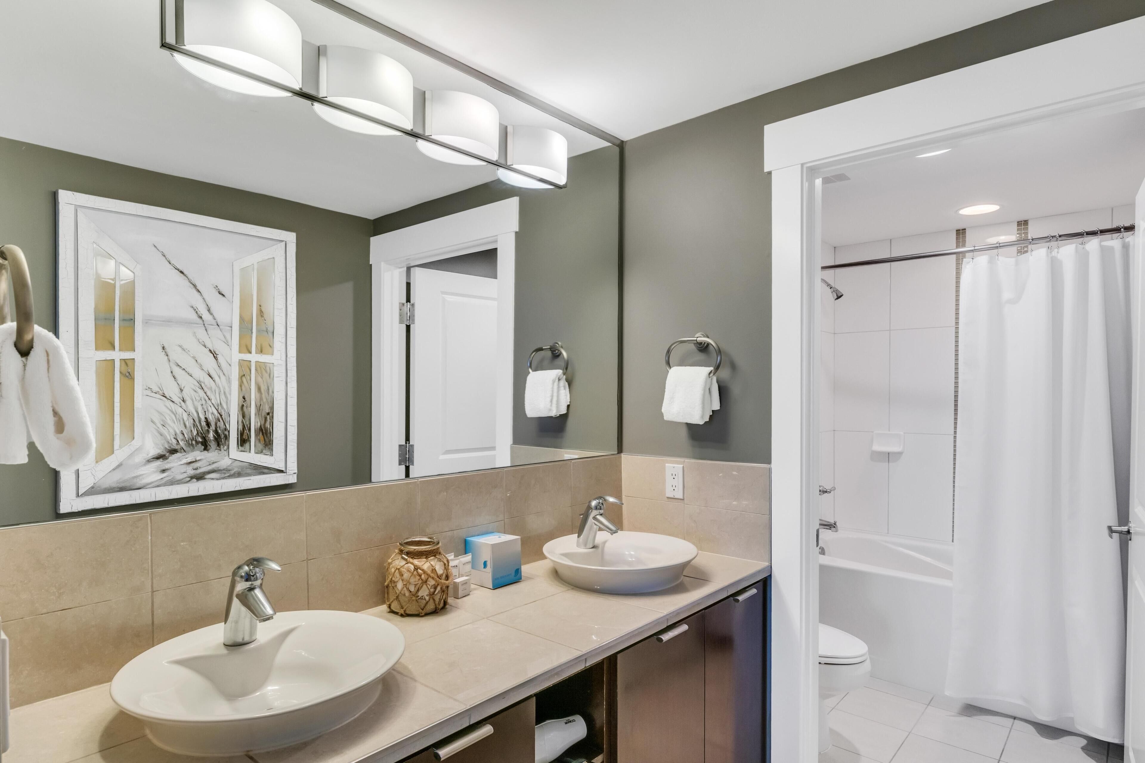 A modern bathroom with two sinks, a large mirror, and a shower area.
