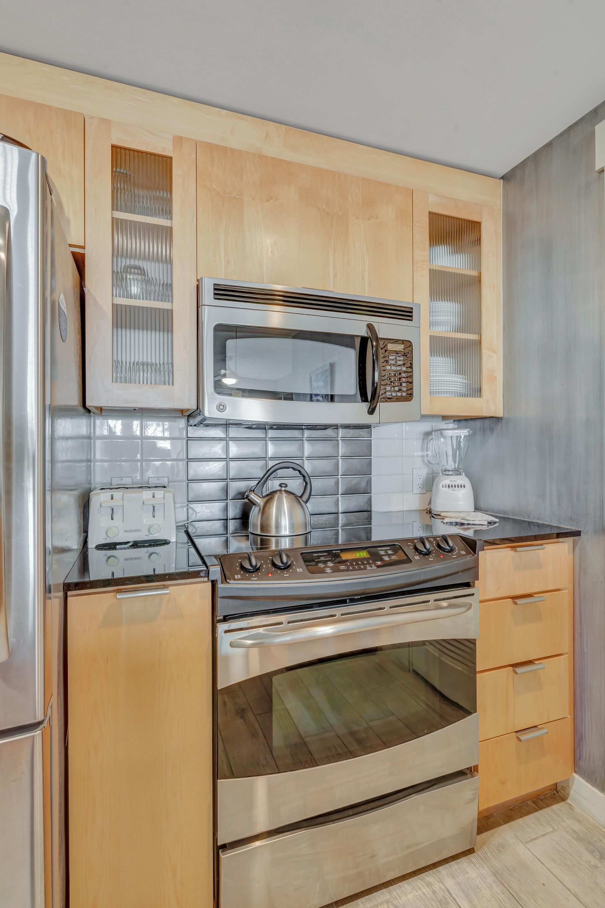 A kitchen with wooden cabinets, a microwave, a stove, a kettle, and a blender.