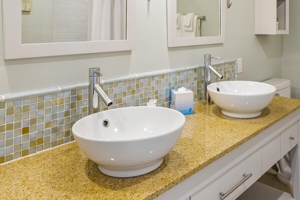 A bathroom with two white ceramic sinks, a mirror above each sink, and a tiled backsplash.