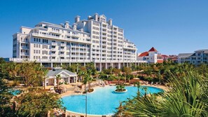 Experience the resort-like atmosphere at this modern hotel, featuring a spacious pool surrounded by lush greenery and comfortable lounge seating.