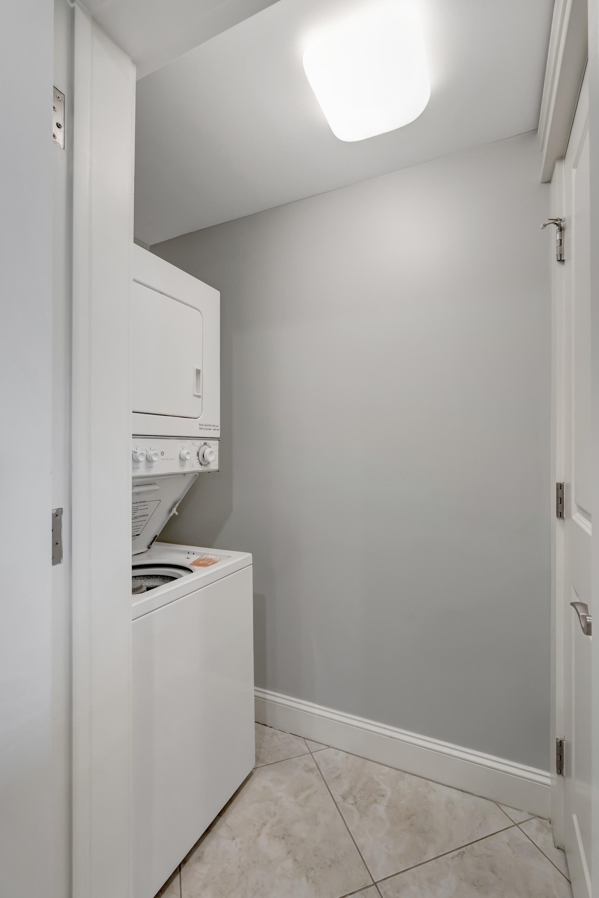 Une buanderie équipée d’un lave-linge et d’un sèche-linge à chargement frontal, d’un sol carrelé et d’une porte donnant sur une autre pièce.