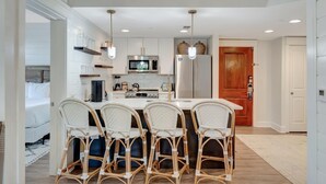 Una cocina moderna con armarios blancos, una isla central con taburetes de bar y electrodomésticos de acero inoxidable.
