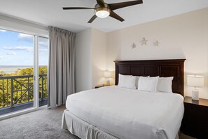 Camera d'albergo con un letto grande, una ventola a soffitto, un comodino con una lampada e vista sull'esterno da un balcone.