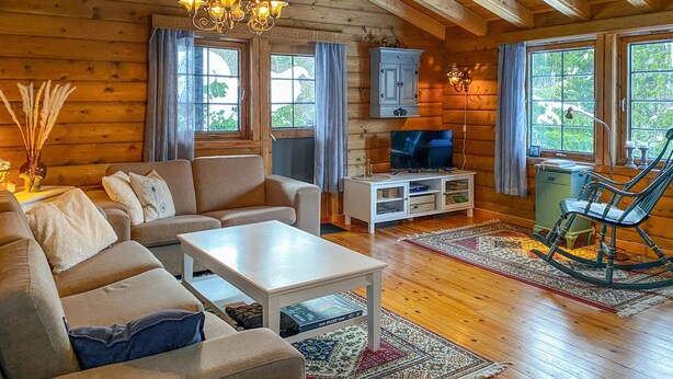 Ein gemütliches Blockhaus-Interieur mit Sofa, Couchtisch, Fernseher und Schaukelstuhl.