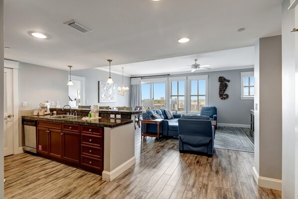 A spacious living area with a large island, dark wood flooring, and a view of the outdoors.