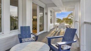 A covered porch with two blue Adirondack chairs, a round table, and a view of the backyard.