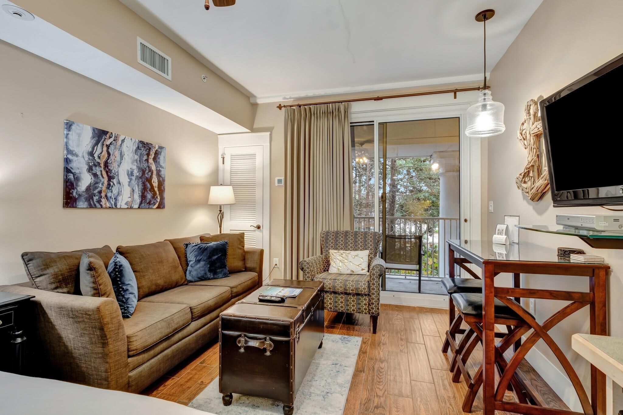 Una sala de estar con un sofá, una mesa de centro y un sillón estampado. Hay un televisor sobre un mueble bajo y una ventana con cortinas.