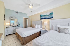 Une chambre d’hôtel avec deux lits, un ventilateur de plafond, un tableau et une commode.