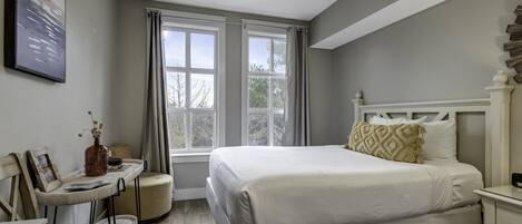 A bedroom with a large bed, a bedside table, a chair, and a window with curtains.
