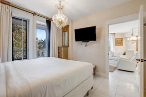 Ein Schlafzimmer mit einem großen Bett, einem an der Wand montierten Fernseher und einem Balkon mit Vorhängen.