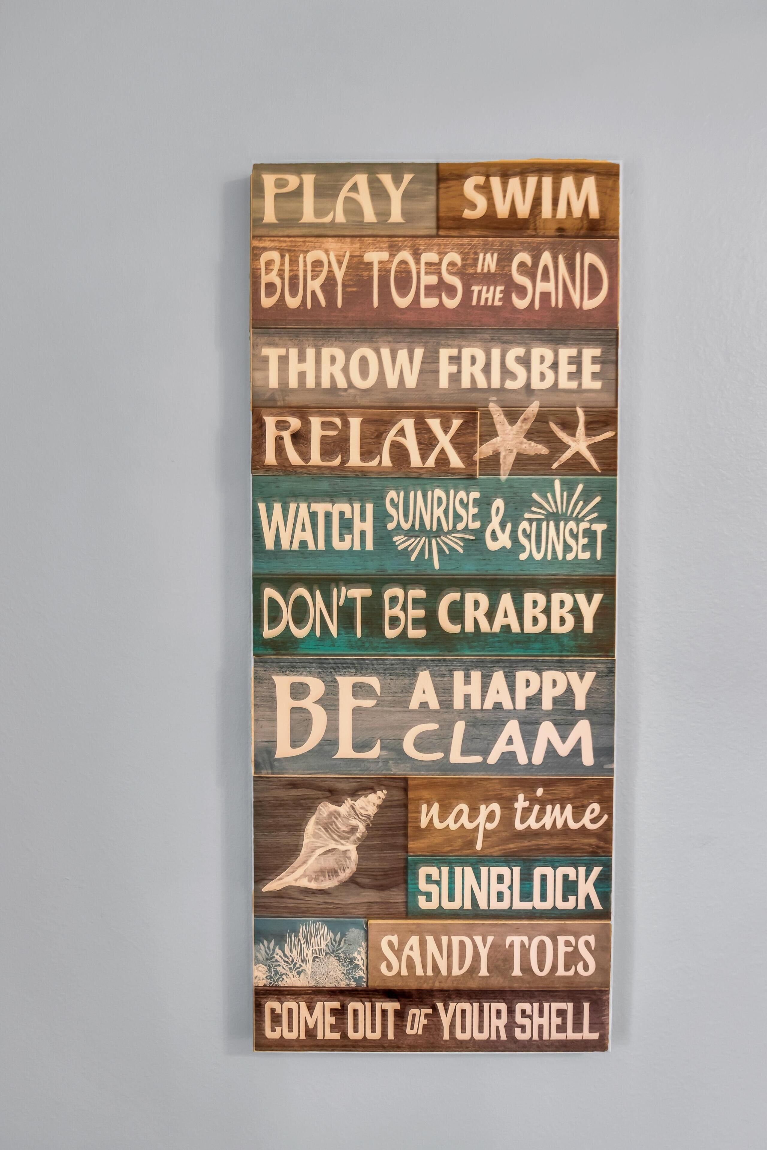A wooden sign with various phrases related to beach activities.