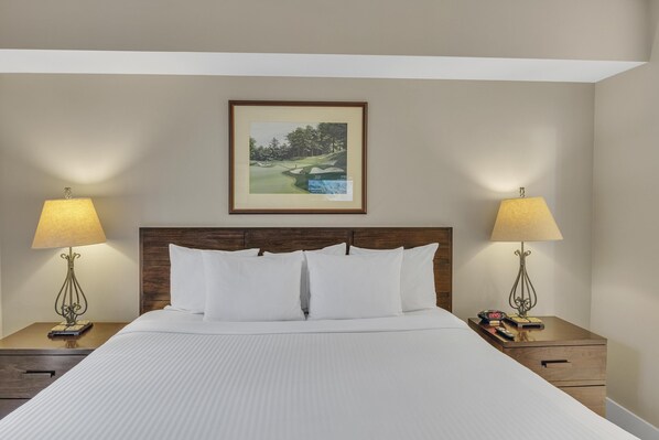 Una cama bien hecha con sábanas blancas, dos lámparas de noche, un cuadro enmarcado de un campo de golf y un cabecero de madera.