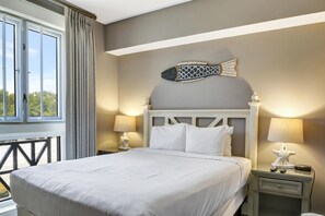 Una cama bien hecha con sábanas blancas, una decoración de peces en la pared y una mesita de noche con una lámpara y un adorno de estrella de mar.