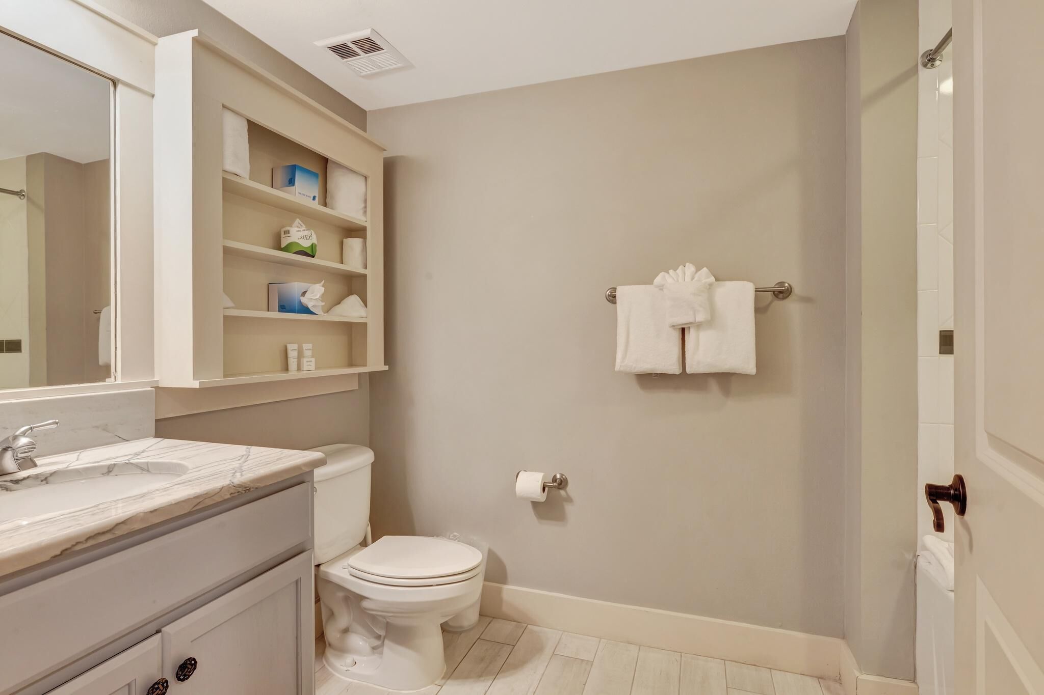 A bathroom with a toilet, sink, and shelves with toiletries.