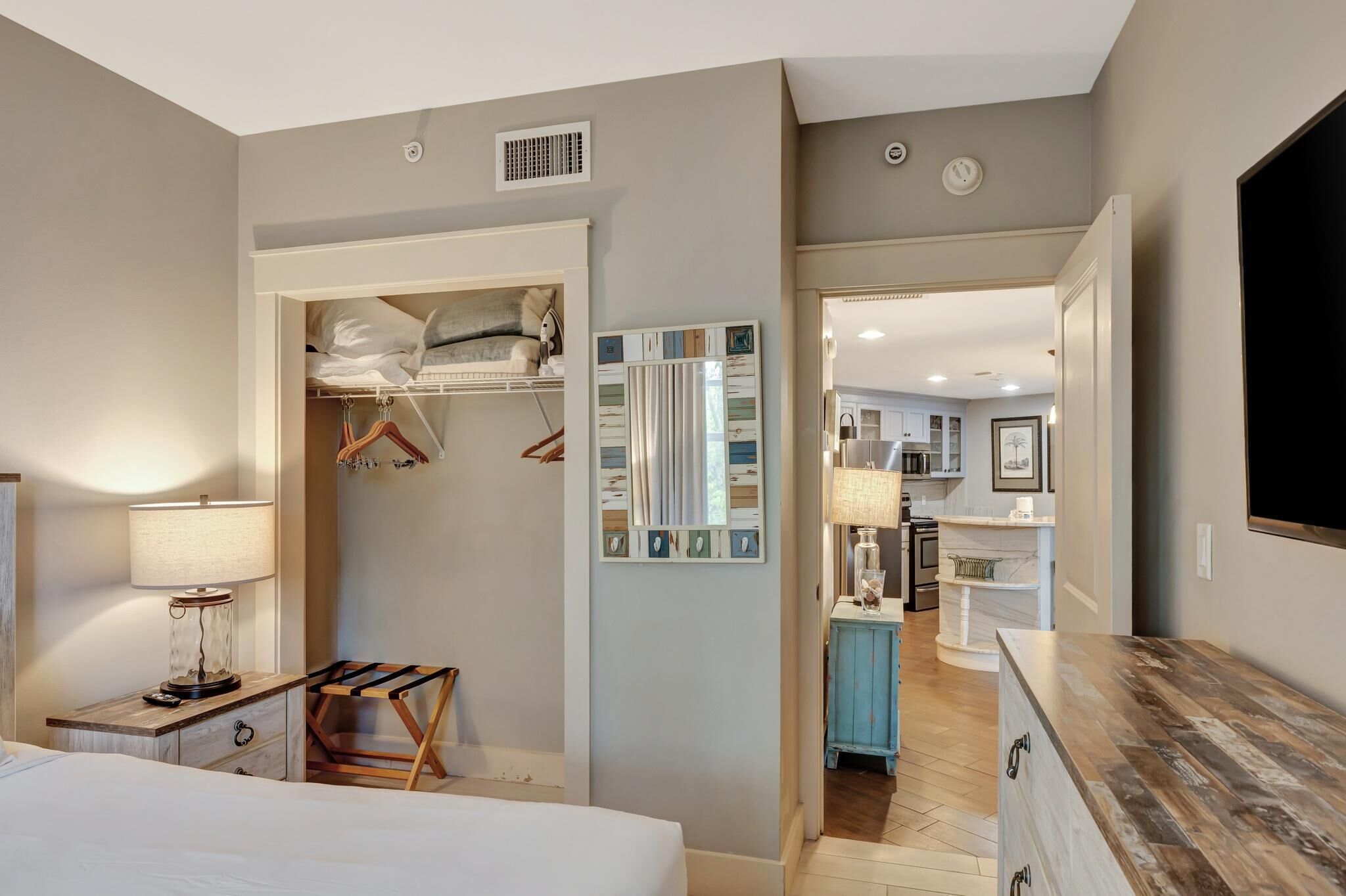 A hotel room with a bed, bedside table, lamp, and a closet with hanging clothes.