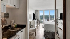 Habitación de hotel con kitchenette, cama, escritorio y balcón con vista a la ciudad.