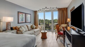 A hotel room with a bed, a sofa, a TV, a dining table, and a balcony with curtains.