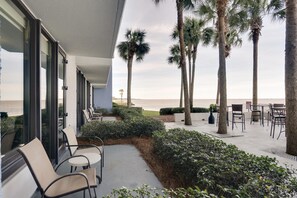 An outdoor patio with chairs and tables, palm trees, and a view of the beach. - Coastal Elegance - Revel in Our King Studio Sanctuary at Sandestin Golf and Beach Resort! (Miramar Beach)