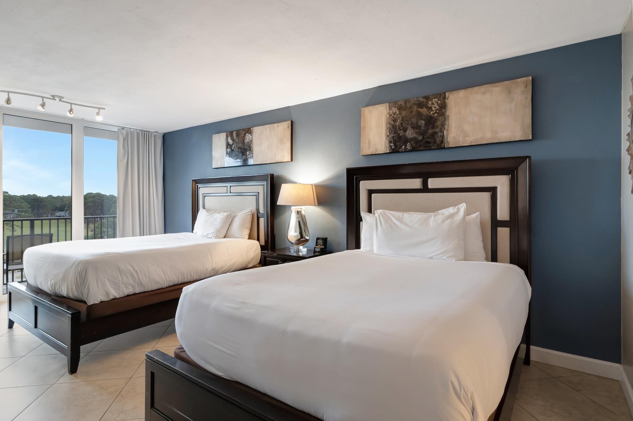 Habitación de hotel con dos camas, un balcón y obras de arte en las paredes.