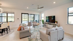 A spacious living room with a large flat-screen TV, two grey sofas, a glass coffee table, and a dining area with a table and chairs. - Alva Vacation Rental w/ Pool & Golf Course Access! (Alva)