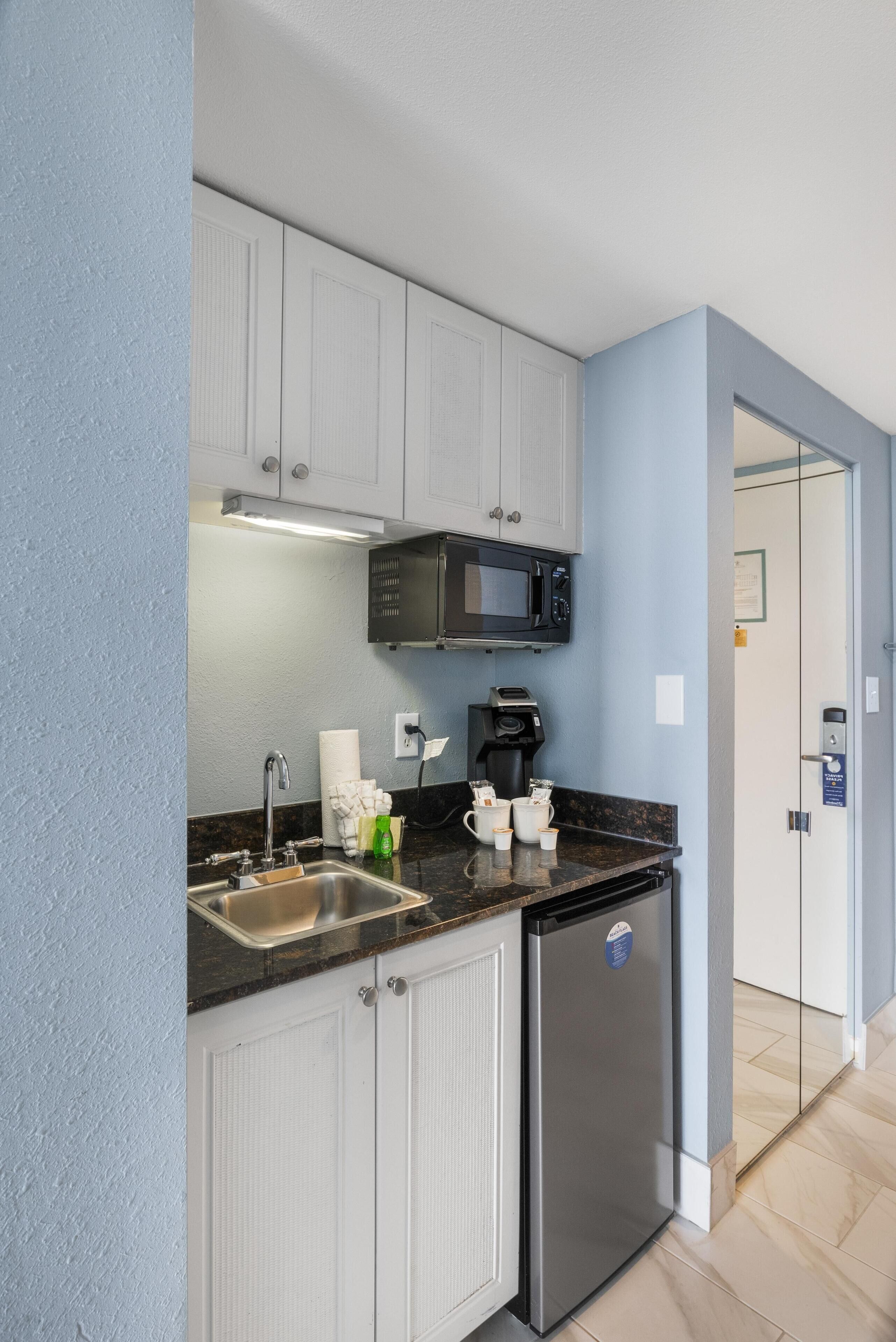 A compact kitchen with white cabinets, a stainless steel refrigerator, a microwave, and a coffee maker.