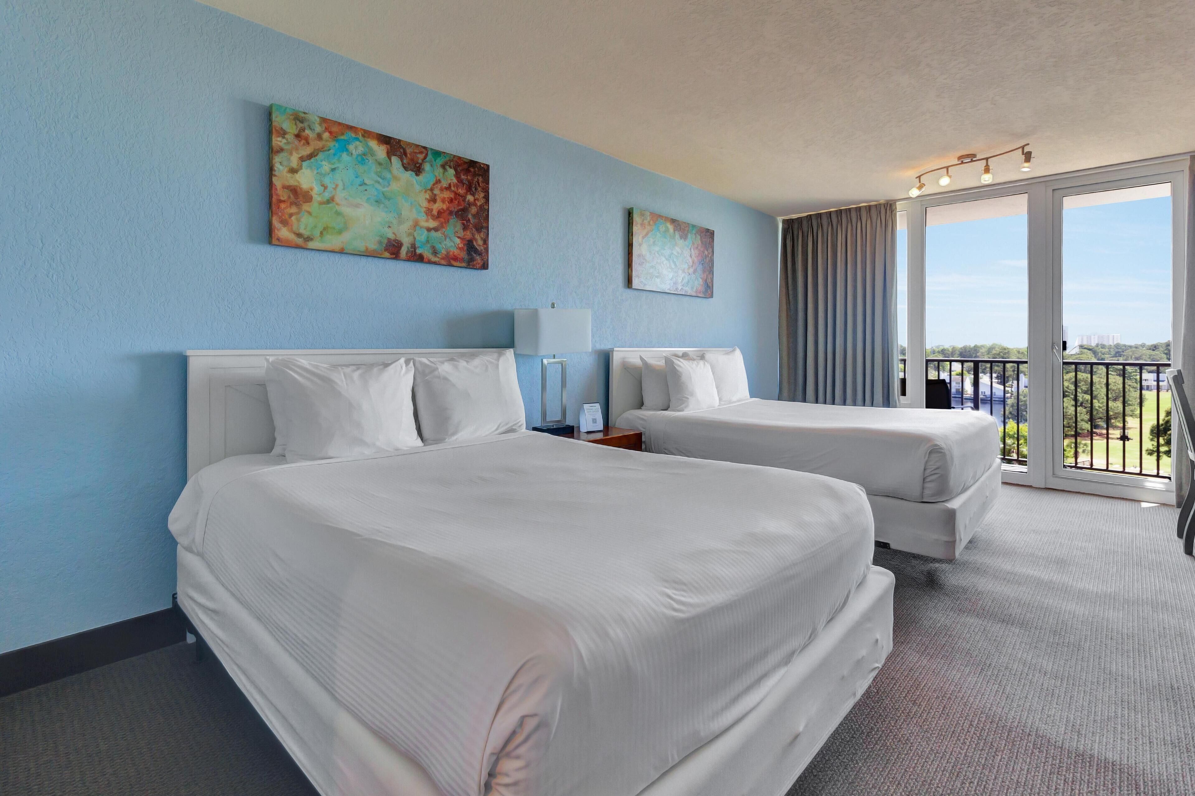 A hotel room with two beds, a large window with a view, and a balcony.
