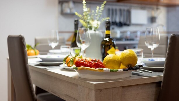 Una mesa de comedor con un plato de fruta, un florero con flores y copas de vino.