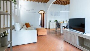 Una sala de estar moderna con sofá, reposapiés, televisor y zona de cocina.