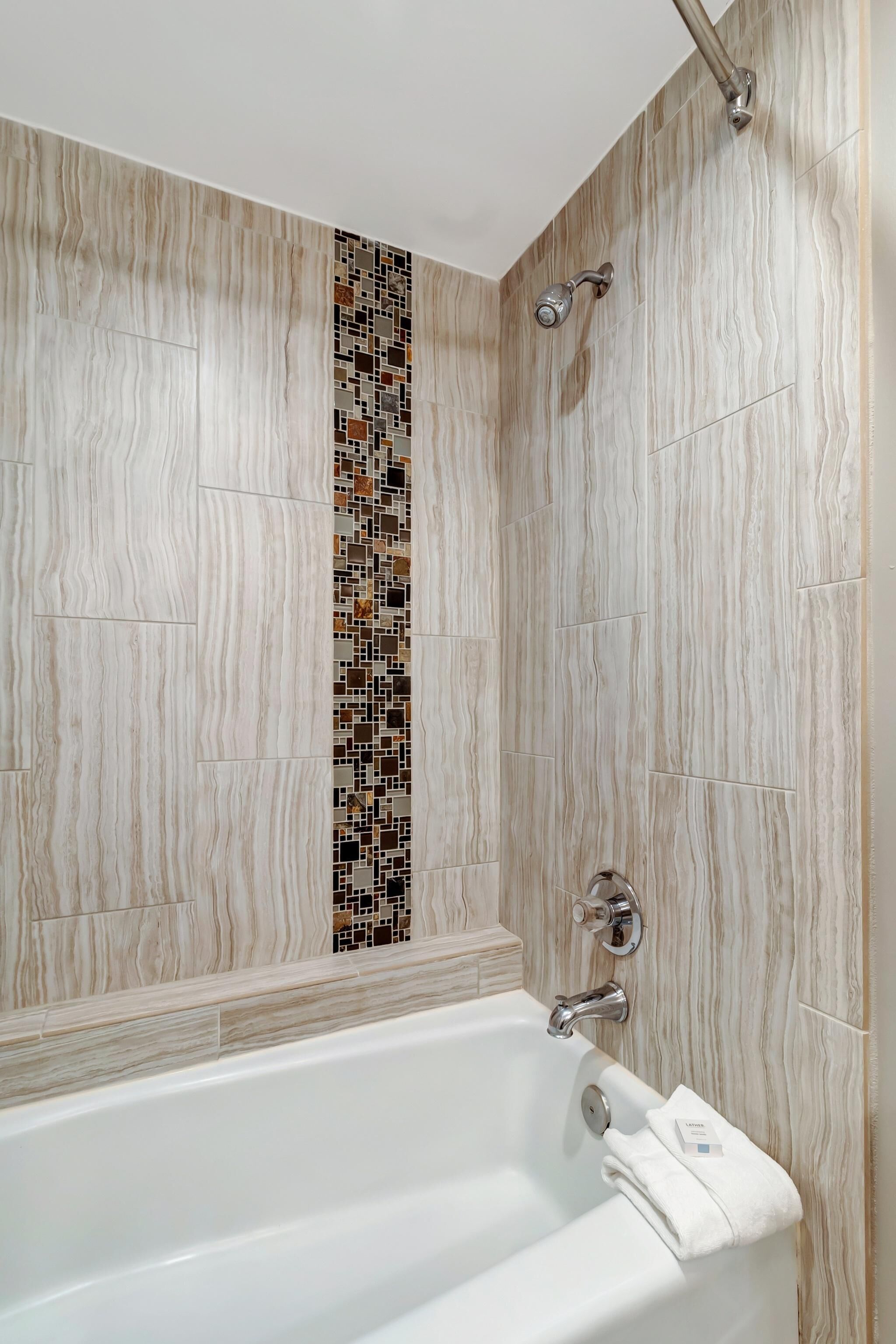 A bathroom with a white bathtub, a shower with a rain showerhead, and a mosaic tile accent wall.
