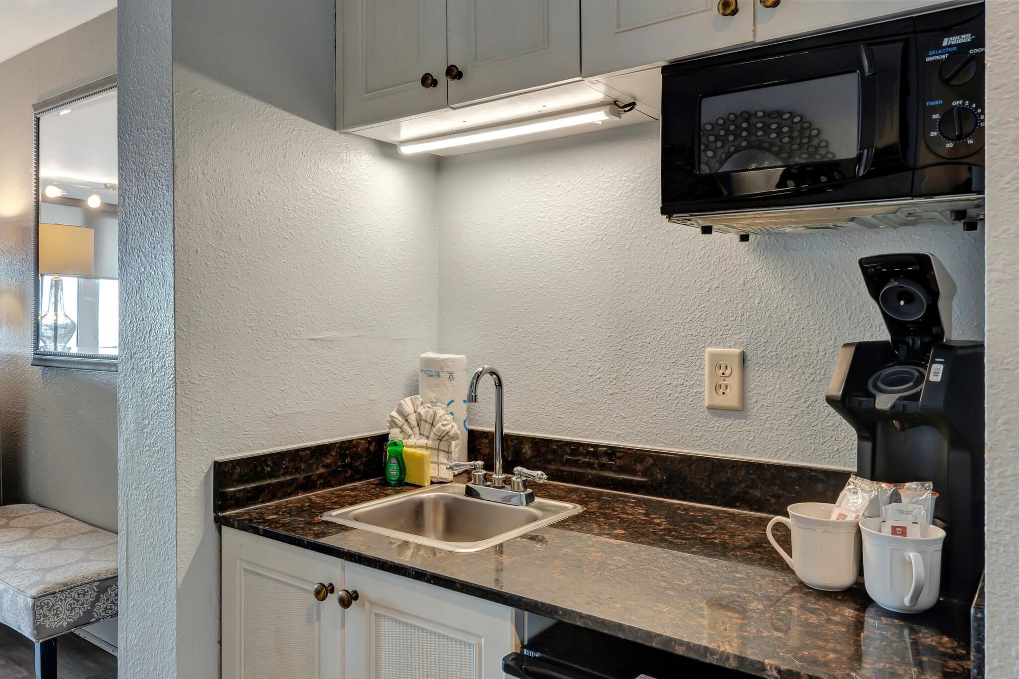 A kitchen with a sink, countertop, microwave, coffee maker, and cabinets.