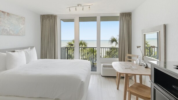Habitación de hotel con cama, escritorio, silla, televisor y balcón con vista al mar.