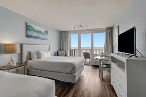 Een hotelkamer met een bed, een bureau, een televisie, een balkon met uitzicht en een schilderij aan de muur.