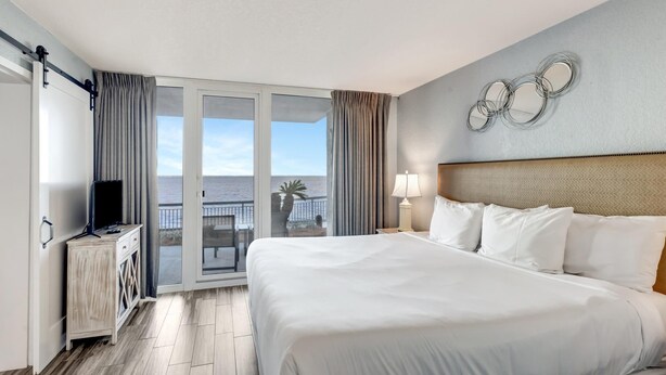 Habitación de hotel con una cama grande, televisión, escritorio y balcón con vista al mar.