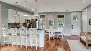 Una cocina moderna con armarios blancos, una isla central con taburetes y luminarias colgantes.
