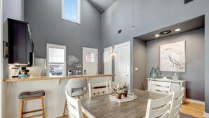 Una cocina moderna con encimera de madera, armarios blancos y un área de comedor con mesa y sillas blancas.