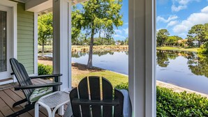 Un portico con due poltrone Adirondack, un tavolino e vista su un lago con alberi e case sullo sfondo.