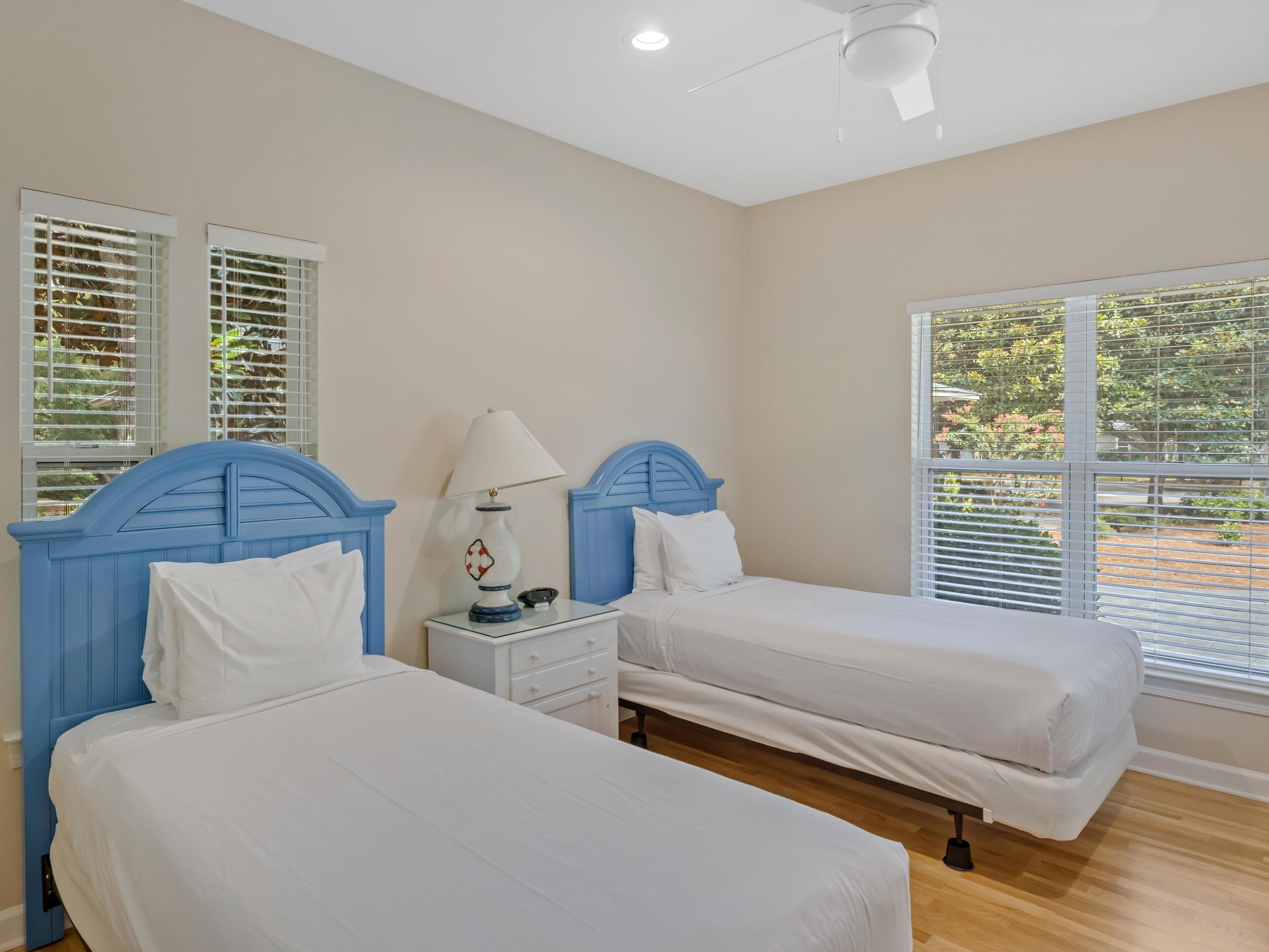 A bedroom with two beds, a nightstand, a lamp, and windows with blinds.