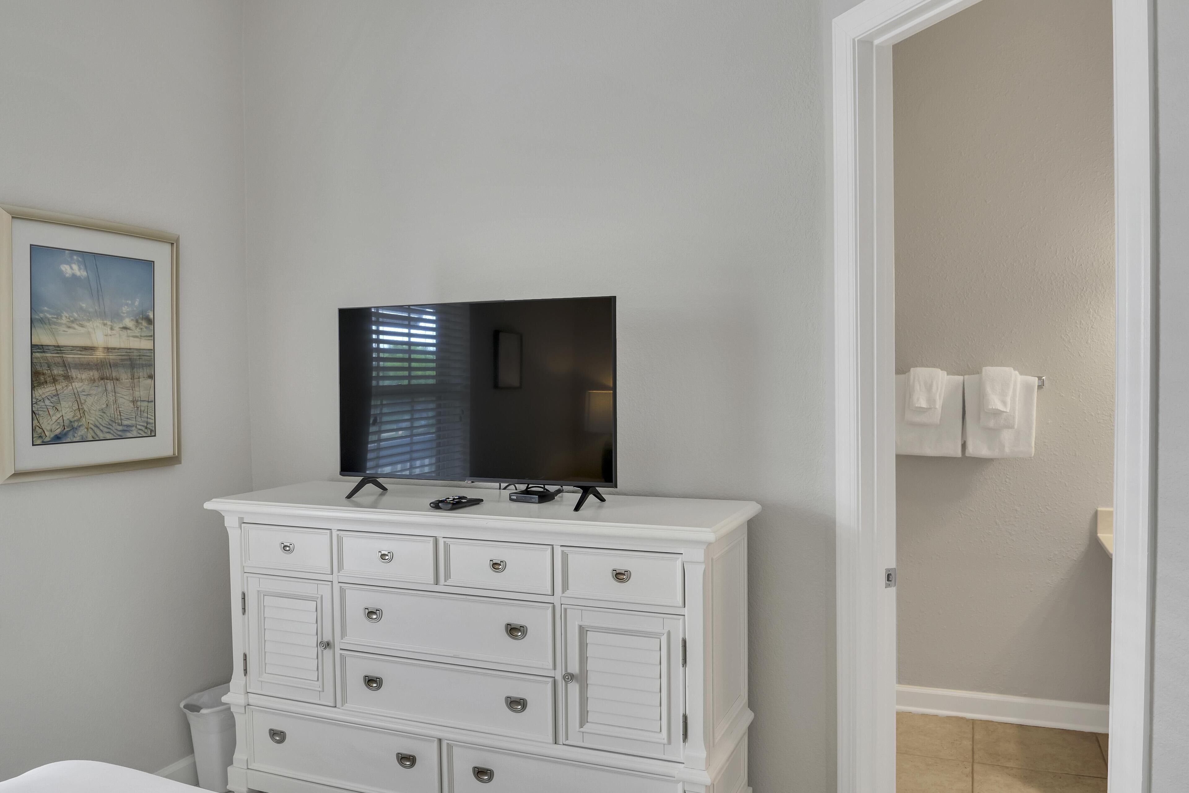 A white dresser with drawers and a flat-screen TV on top.