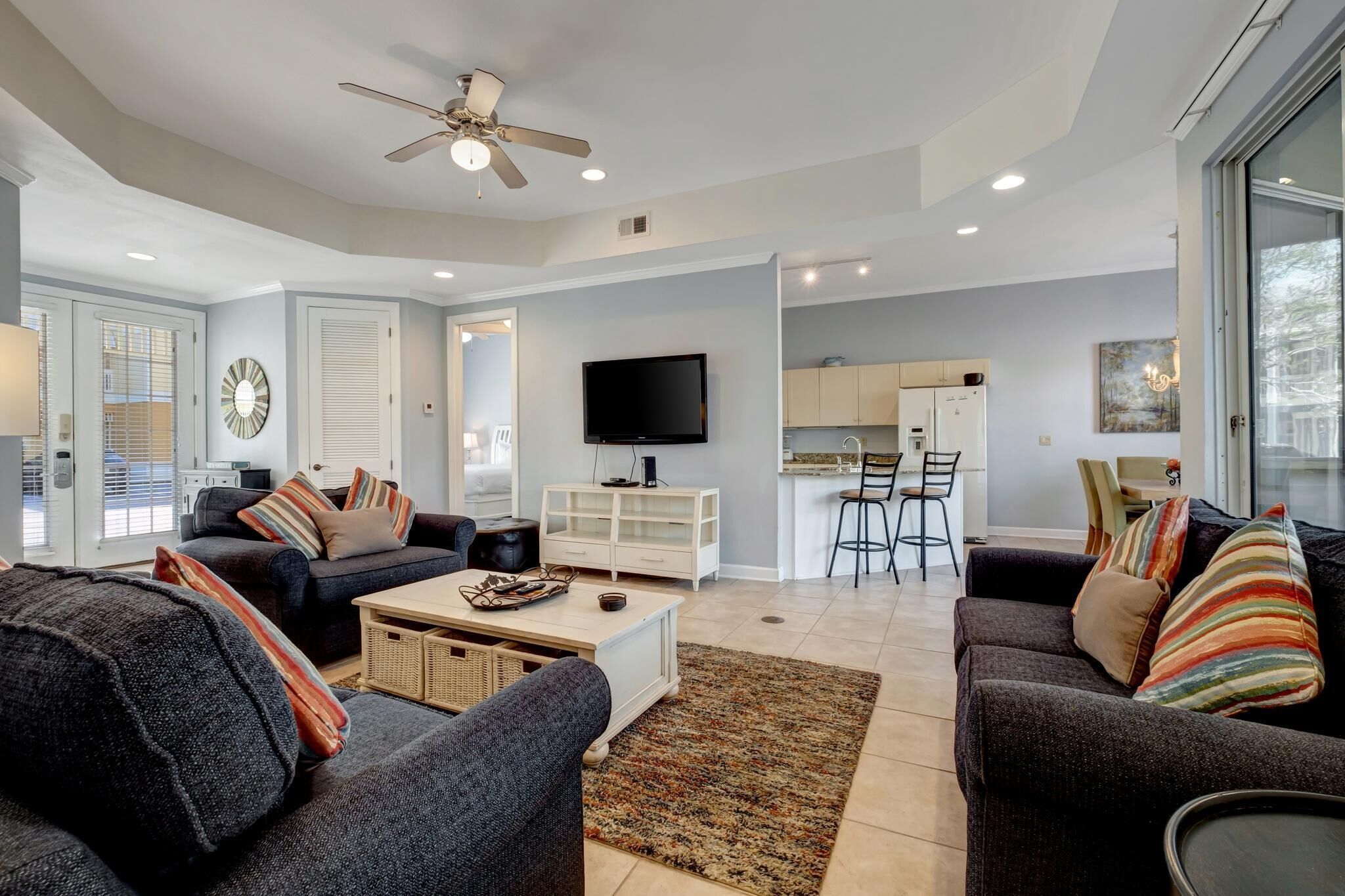 A modern living room with a sofa set, a coffee table, and a television. There is a kitchen area with a bar and a dining table.