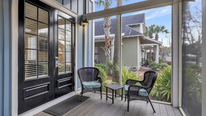 A covered porch with two wicker chairs and a small table, overlooking a residential area with palm trees and a house. - Spacious 3BR/3BA Family Retreat for 8 at Sandestin Golf and Beach Resort! (Miramar Beach)