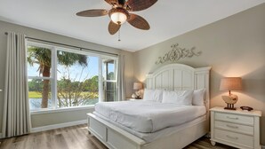 Une chambre avec un grand lit, un ventilateur de plafond, une table de chevet et une vue sur l’extérieur.