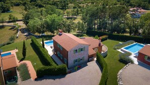 Ett stort hus med en swimmingpool, omgivet av välskötta trädgårdar och med utsikt över ett skogsområde.