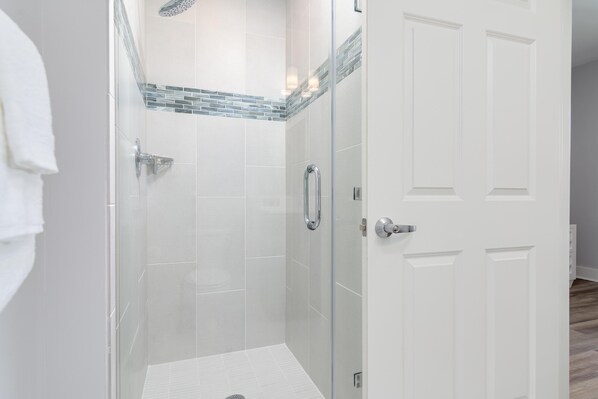 A modern bathroom with a glass shower enclosure, white tiled walls, and a white door.