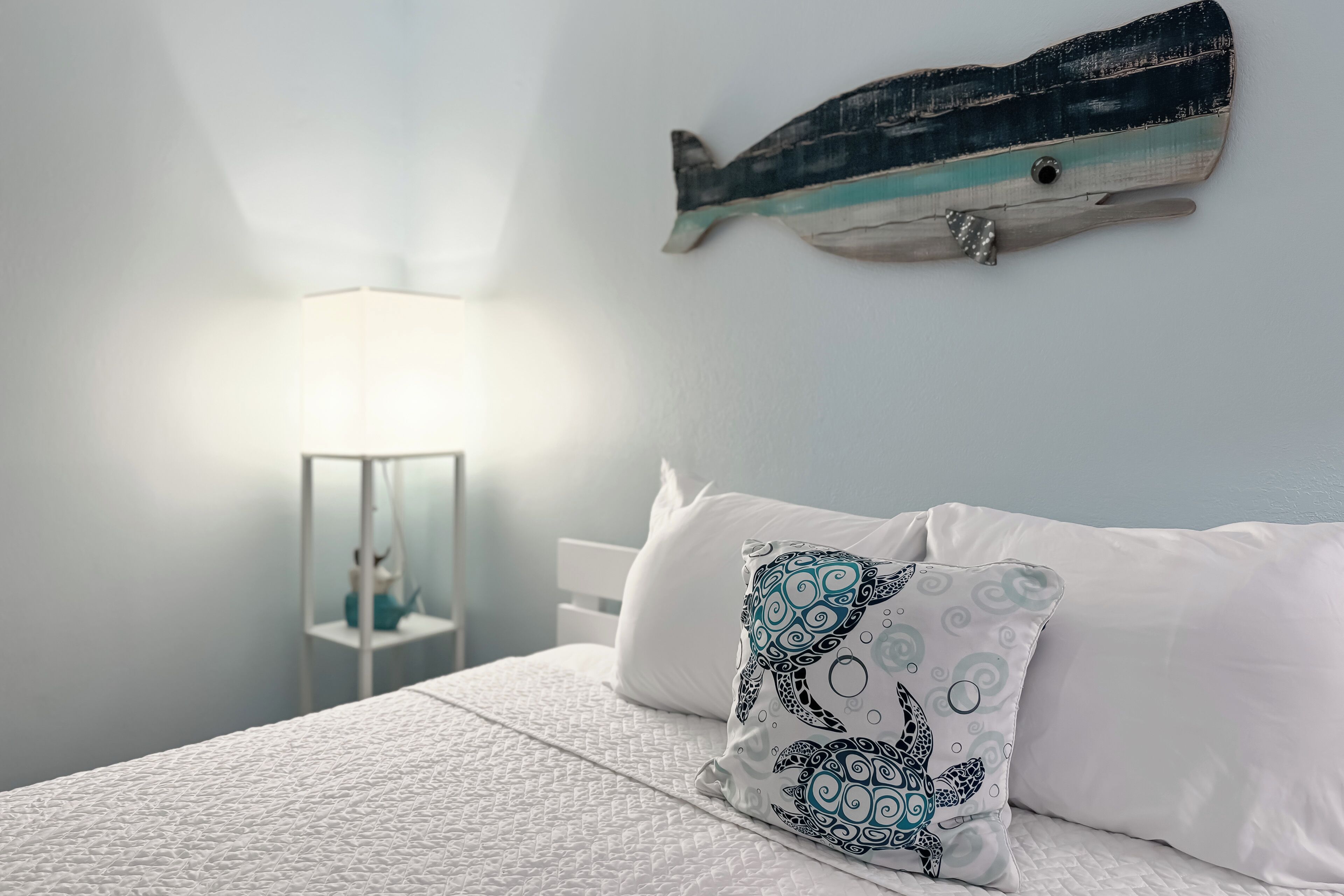 Une chambre à coucher avec un lit, du linge de lit blanc, une décoration murale représentant des poissons et une lampe de chevet.