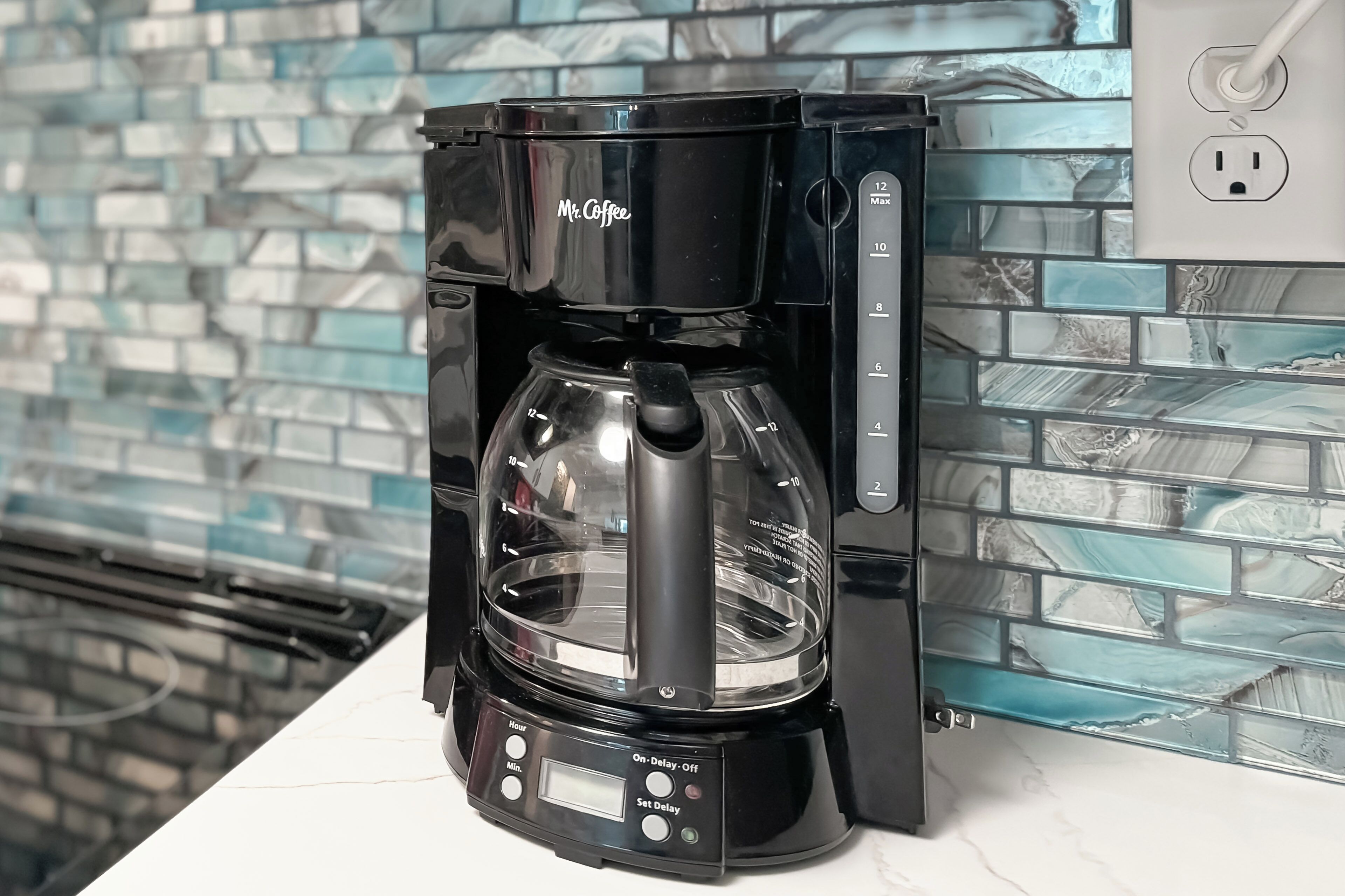 A black Mr. Coffee coffee maker on a kitchen counter with a tiled backsplash.