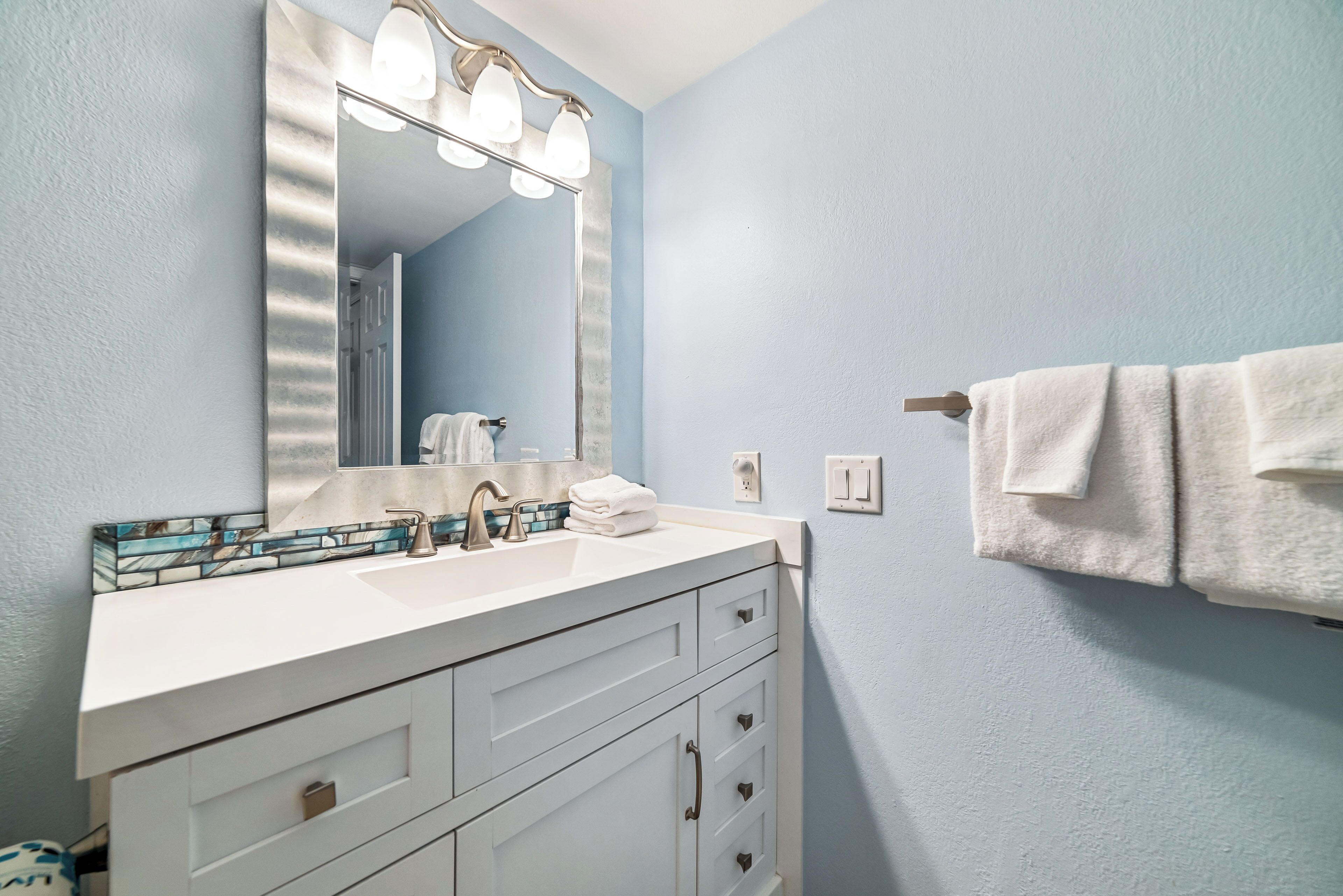 A bathroom with a white vanity, a large mirror, and a towel rack.