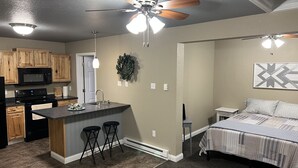 A compact apartment with a kitchenette, a dining area, and a bedroom. - The Petite Perch (Alden)