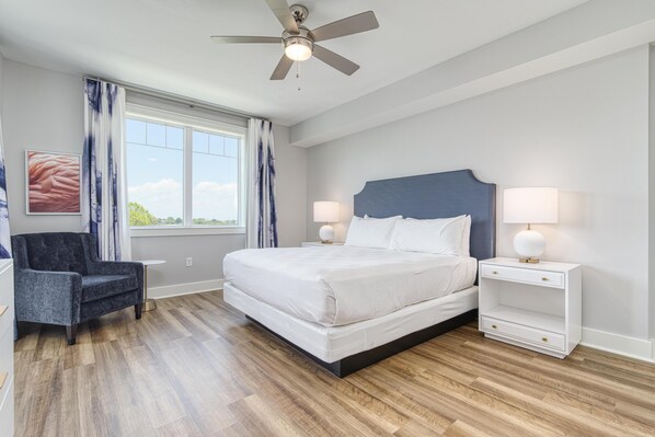 A bedroom with a bed, nightstands, a chair, a ceiling fan, and a window with curtains.