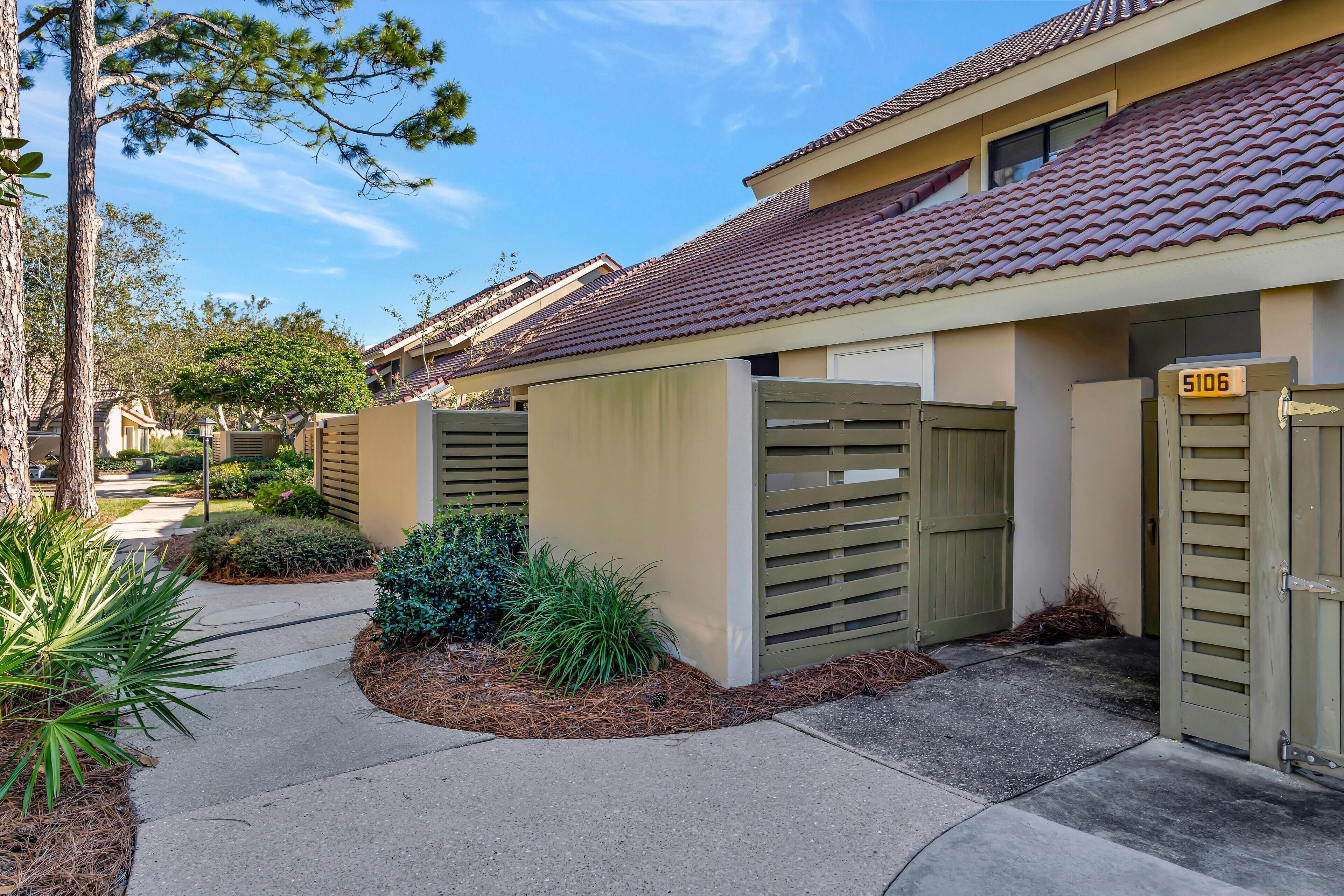 A residential building with a gated entrance, numbered 5106, and a well-maintained garden area with various plants.